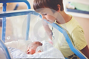 Beautiful newborn baby boy, laying in crib in prenatal hospital, his brothers looking at him