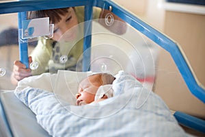 Beautiful newborn baby boy, laying in crib in prenatal hospital, his brothers looking at him