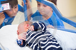 Beautiful newborn baby boy, laying in crib in prenatal hospital, his brothers looking at him