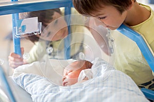 Beautiful newborn baby boy, laying in crib in prenatal hospital, his brothers looking at him