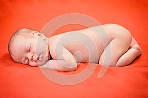 Beautiful newborn baby boy sleeping peacefully on the soft red blanket