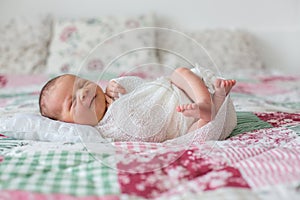 Beautiful newborn baby boy, widely smiling, wrapped in wrap, lying down in bed