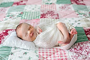 Beautiful newborn baby boy, widely smiling, wrapped in wrap, lying down in bed