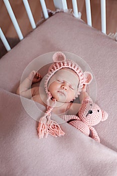 Beautiful newborn baby girl wearing pink hat and peacefully sleeping in her bed.
