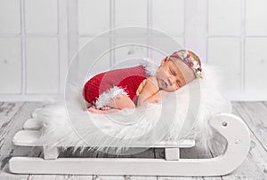 Beautiful newborn in red romper on sleigh cot