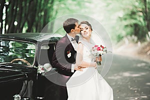 Beautiful newlywed couple posing near retro black car