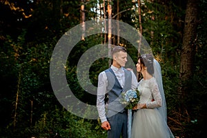 Beautiful newlyweds couple walking in the woods. Honeymooners. Bride and groom holding hand in pine forest, photo for Valentine`s