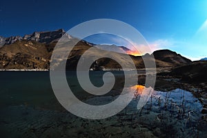 A beautiful night landscape with a reflection of rocks in a mountain lake with the burning mountains in the background