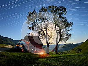 Beautiful night scene startrails with a family camping with a car and a tent and camp fire in the wild Apuseni mountains, Transylv