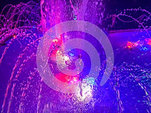A beautiful night singing fountain with jets of water and splashes with multi-colored illumination. The background