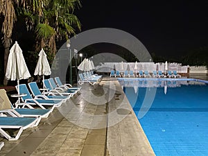 Beautiful night swimming pool with umbrellas and deck chairs and palm trees in a hotel on vacation in a tourist warm tropical