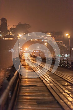 Beautiful night time of silhouette traveler walking on the Mon wooden bridge with beautiful reflections of Sangkhlaburi