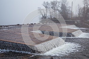 A beautiful Norwegian autumn scenery. Misty morning on a lake. Water flowing over the dam, waterfall.