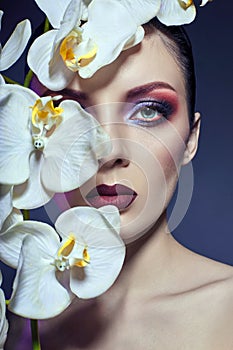 Beautiful Nude woman with a branch of white Orchid in her hands, bright contrasting makeup on the eyes and lips. Contrasting colo