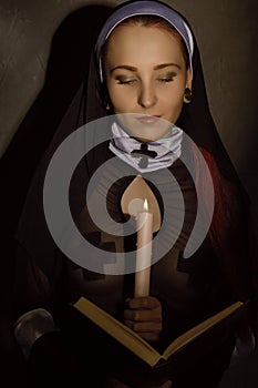 Beautiful nun with a candle reading the Bible. religious concept