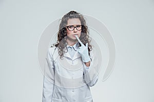 Beautiful nurse with black hair. Wearing blue medical uniformed handbags. In black glasses and gloves on a gray