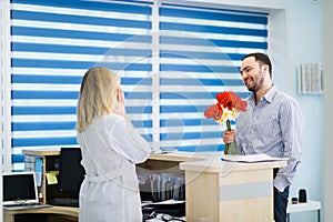Beautiful nurse lady flirting with a handsome male client. He brought her flowers to work.