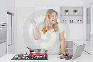 Beautiful obese woman with laptop in the kitchen