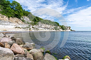 Beautiful ocean landscape with steep white chalkstone cliffs and forest and rocks in the foreground and sea kayakers approaching