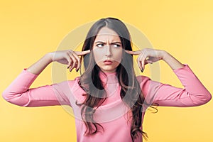 Beautiful offended woman covering her ears with fingers isolated on yellow background