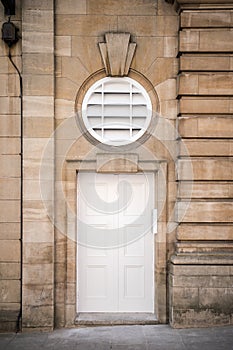 Beautiful old Art Deco white external door set in stone wall with circle feature and keystones above doorway. Restored circular photo