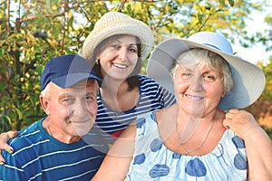 Beautiful old couple is sitting on the bench in the park with their adult daughter. Grandma and grandpa are hugging and smiling.