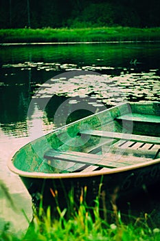 A beautiful old fishing boat is floating along a grassy riverbank on a sunny summer day. Nostalgia, tranquility, and the peaceful