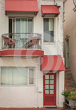 Beautiful old house with windows and balcony with flower pots. White house facade with red color door and windows