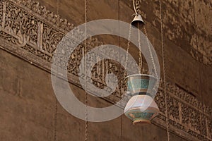 A beautiful old lantern hanging from the ceiling and Arabic writing on the wall of sultan Hassan mosque