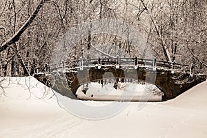 Beautiful old stone bridge of winter forest in the snow at sunset frosty days. Trees covered in frost and snow.