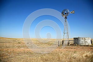 A beautiful old windmill water tower in a field on a beautiful summer day with a cloudless blue sky in a field