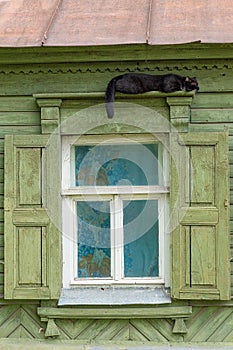 A beautiful old window with beautifully designed platbands window with open shutters. Black cat sleeps on the platband