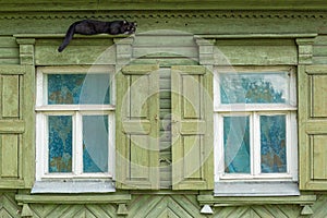 A beautiful old window with beautifully designed platbands window with open shutters. Black cat sleeps on the platband