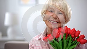 Beautiful old woman with bunch of flowers smiling at camera, birthday gift