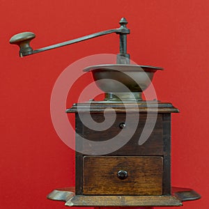 A beautiful old wooden coffee grinder against a solid red background
