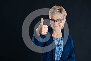 Beautiful older secretary showing thumbs up and smiling  to the camera