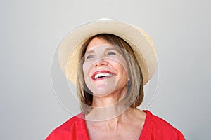 Beautiful older woman laughing with hat against gray wall