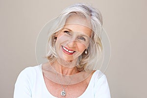 Beautiful older woman smiling and standing by wall