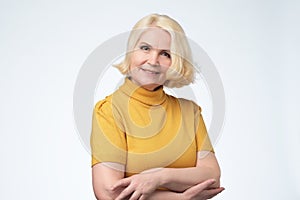 Beautiful older woman smiling and standing by wall