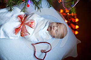 One week old newborn baby wrapped in blanket near Christmas tree