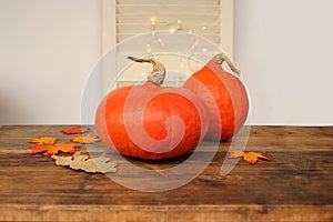 Beautiful orange pumpkins on a wooden table among the leaves on a light background with luminous garlands, a symbol of the autumn