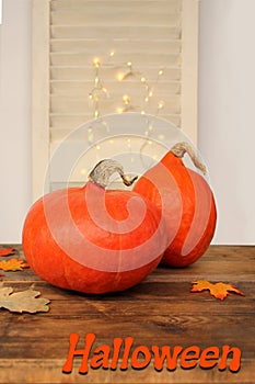 Beautiful orange pumpkins on a wooden table among the leaves on a light background with luminous garlands, a symbol of the autumn