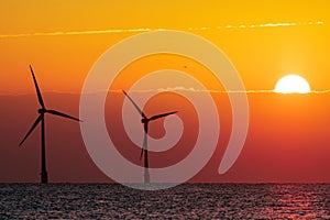 Beautiful orange sunrise behind offshore wind farm turbines