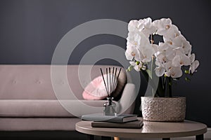 Beautiful orchid, books and air reed freshener on table indoors