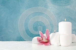 Beautiful orchid candles and spa stones on white table, space for text