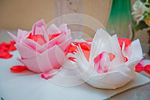 Beautiful origami flower made of napkin on white background . Petals of a red rose . White and pink flowers on napkins.