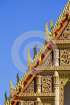 Beautiful ornamental golden Gable Apex on rooftop of traditional Thai temple with blue sky