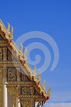 Beautiful ornamental golden Gable Apex on rooftop of traditional Thai temple with blue sky