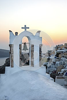 Arch with a bell, white houses and church with blue domes in Oia or Ia at golden sunset, island Santorini, Greece. - Immagine photo