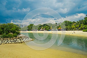 Beautiful outdoor view of unidentified poople enjoying the yellow sand and tropical beach in sentosa and swimming in a